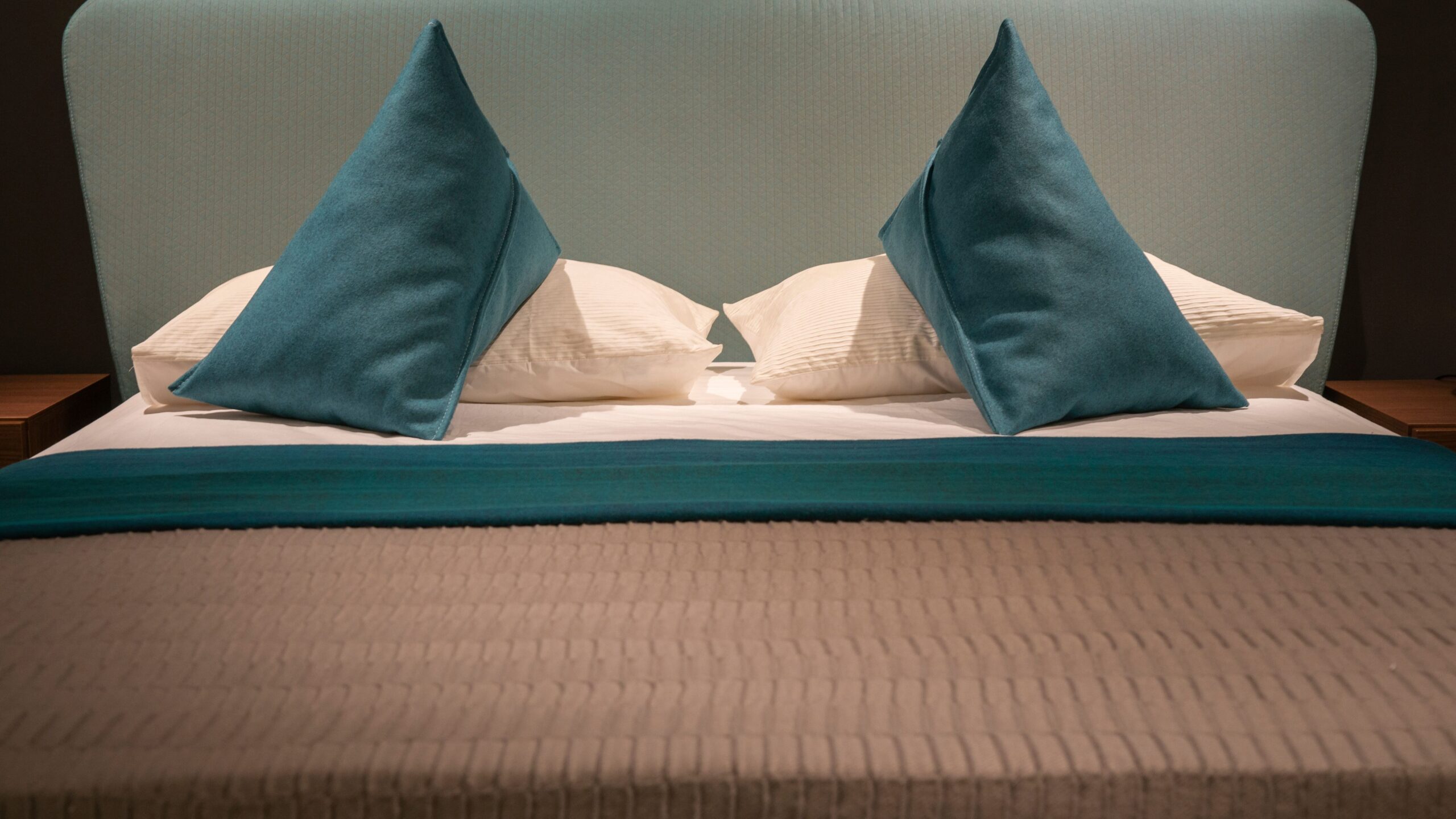 Modern minimalist bed with teal pillows and headboard, showcasing elegant interior design.
